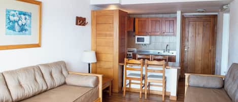 Un espacio habitable compacto con sofá, una mesa de comedor con sillas, una zona de cocina con armarios de madera y un microondas, y un cuadro en la pared.