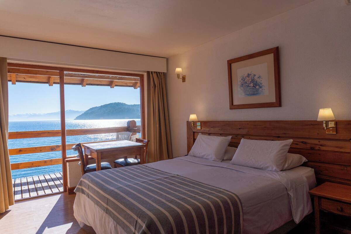 A hotel room with a bed, a desk, and a view of the sea.
