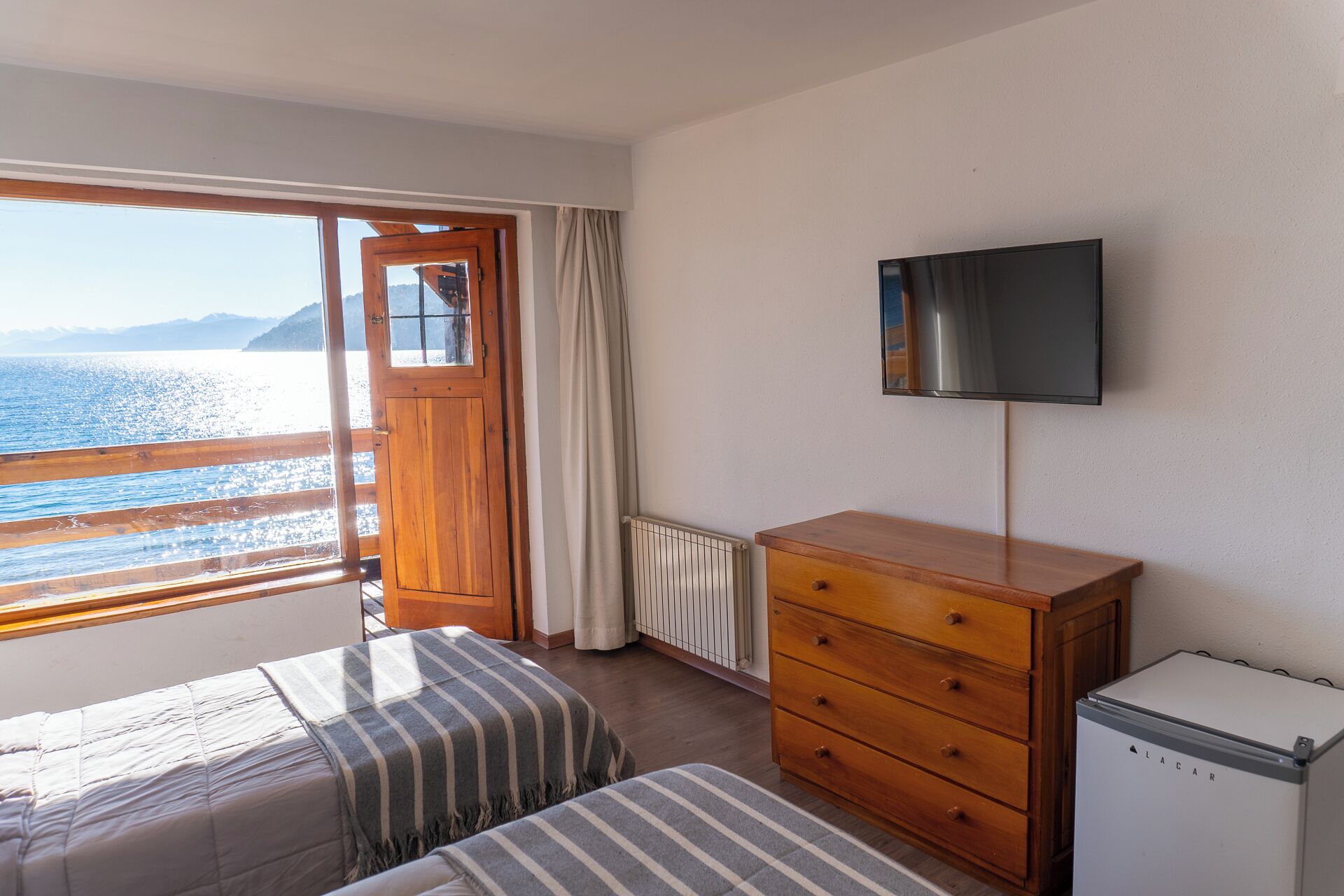 Un dormitorio con un aparador de madera, un televisor, una cama con manta a rayas y vistas al mar.