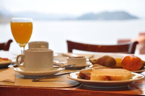 Una mesa de desayuno con un vaso de jugo de naranja, una taza, un plato con tostadas y un plato con fruta.