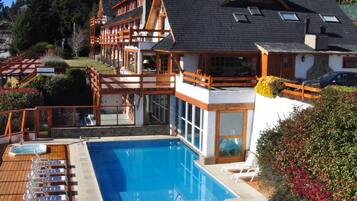 Un resort con piscina, terraza de madera, sillas de descanso y montañas al fondo.