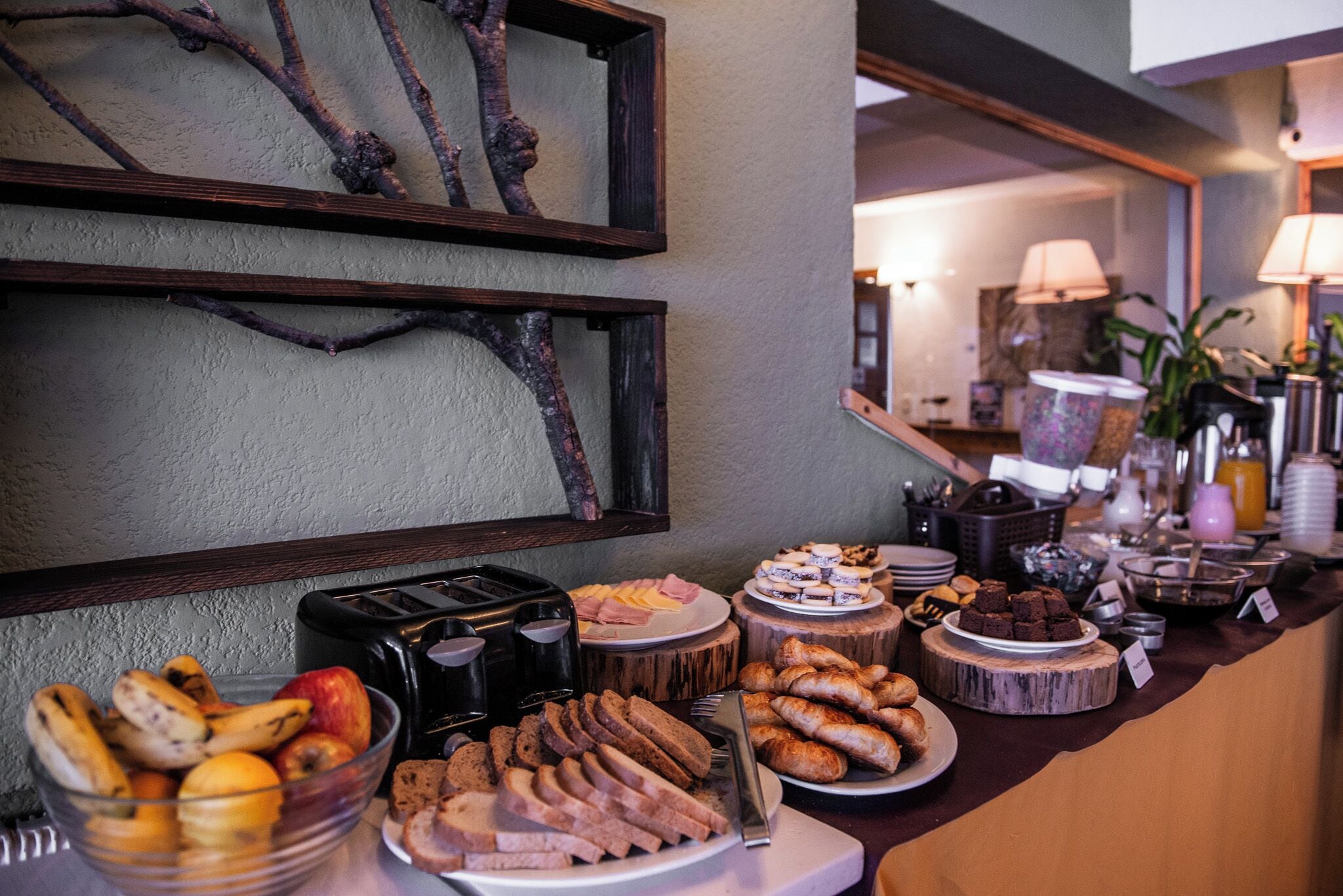 A buffet with various food items, including fruits, breads, and desserts, arranged on a counter with a rustic design.