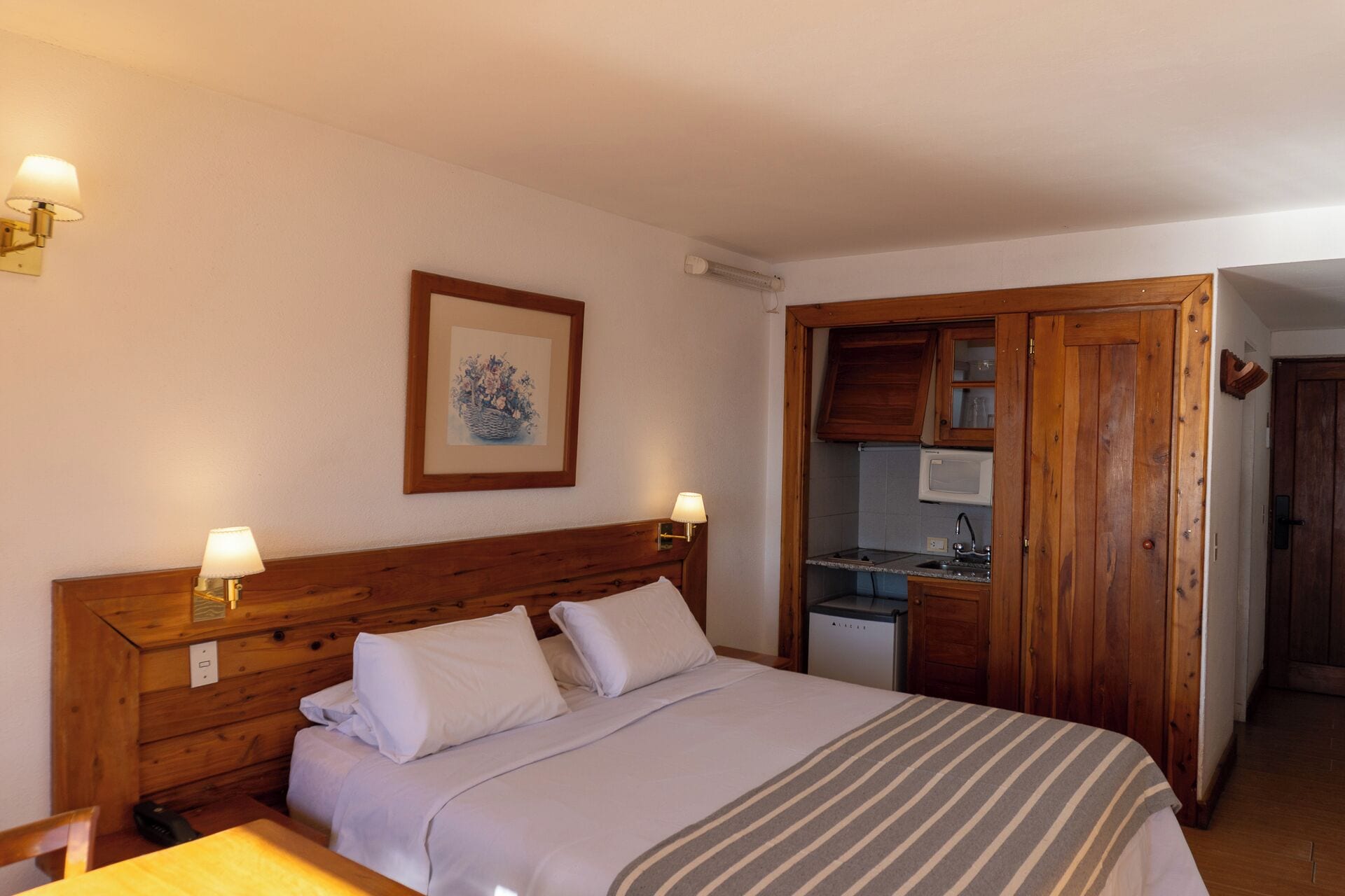 A bedroom with a wooden headboard, a bed with white linens, two bedside lamps, and a framed picture on the wall.