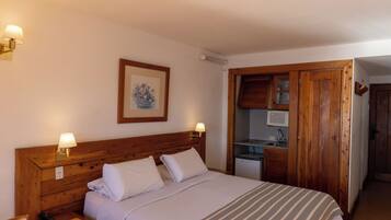 A bedroom with a wooden headboard, a bed with white linens, two bedside lamps, and a framed picture on the wall.