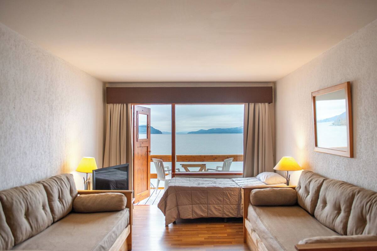 A hotel room with a bed, two sofas, a TV, and a view of the sea.