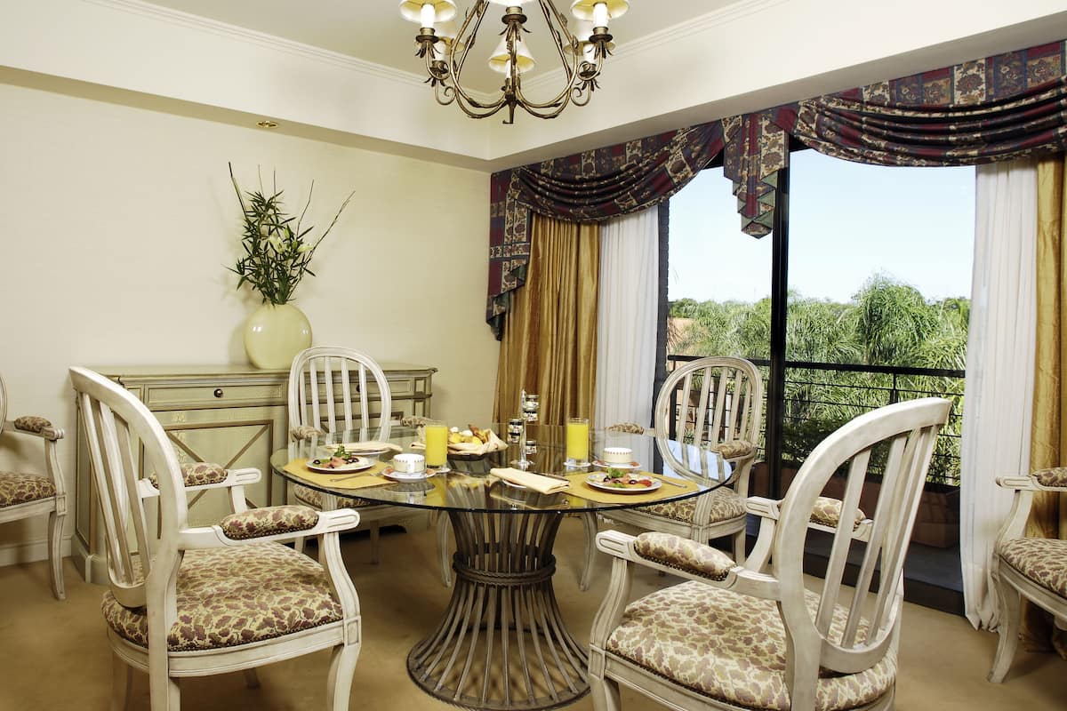 Une salle à manger avec une table ronde en verre, entourée de six chaises rembourrées ornées de motifs floraux.