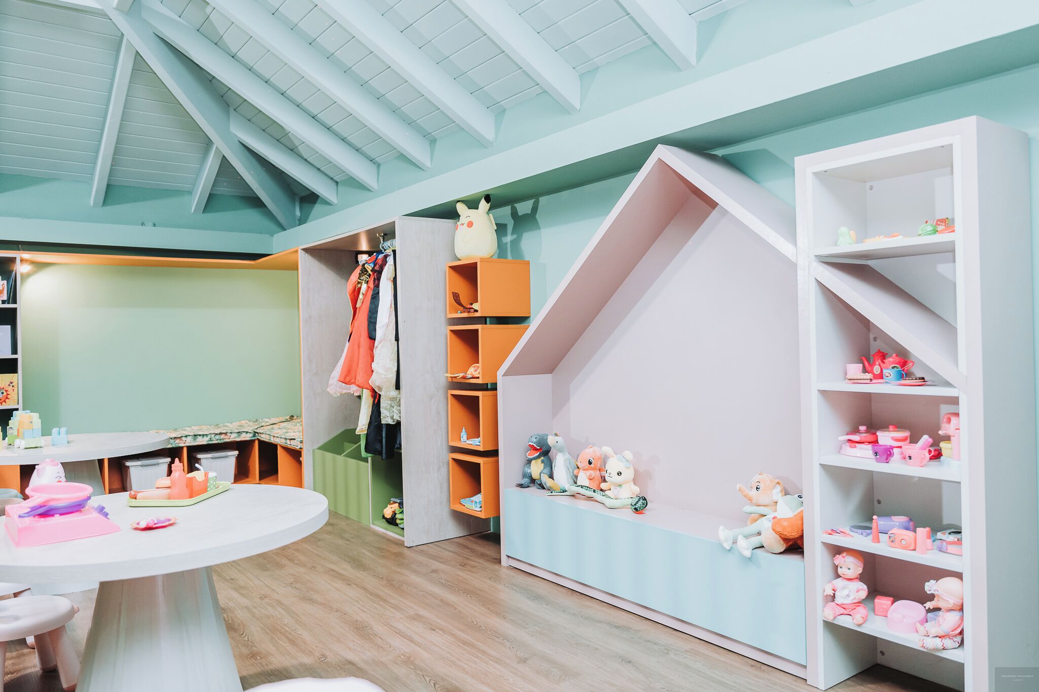 Ein Spielzimmer mit rundem Tisch, Regalen voller Spielzeug und einem Hochbett.