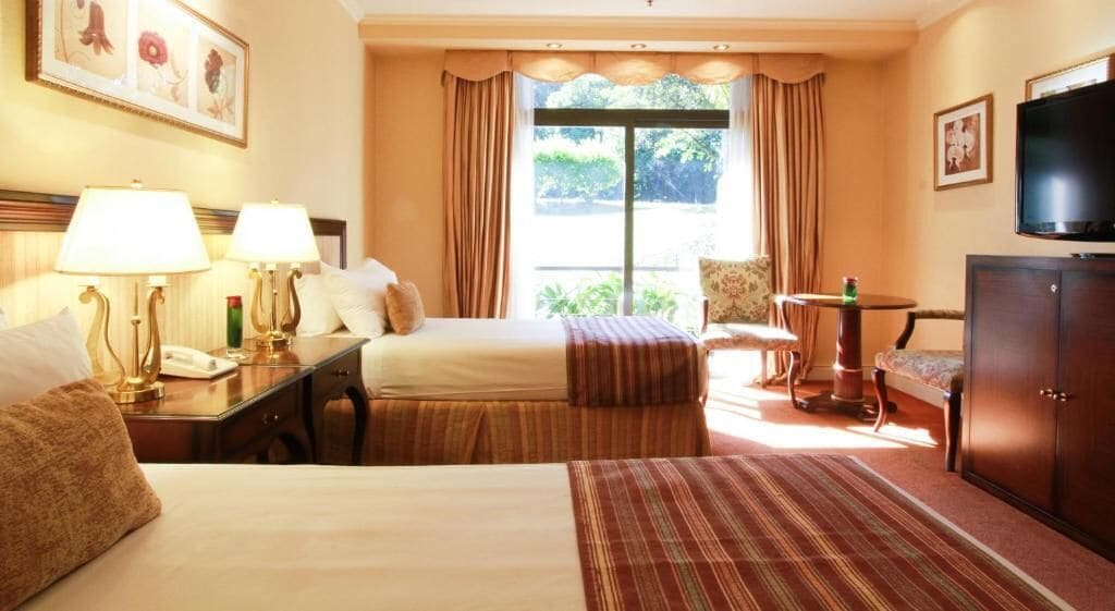 Habitación de hotel con dos camas, un escritorio con teléfono, televisión y vistas a zonas verdes.