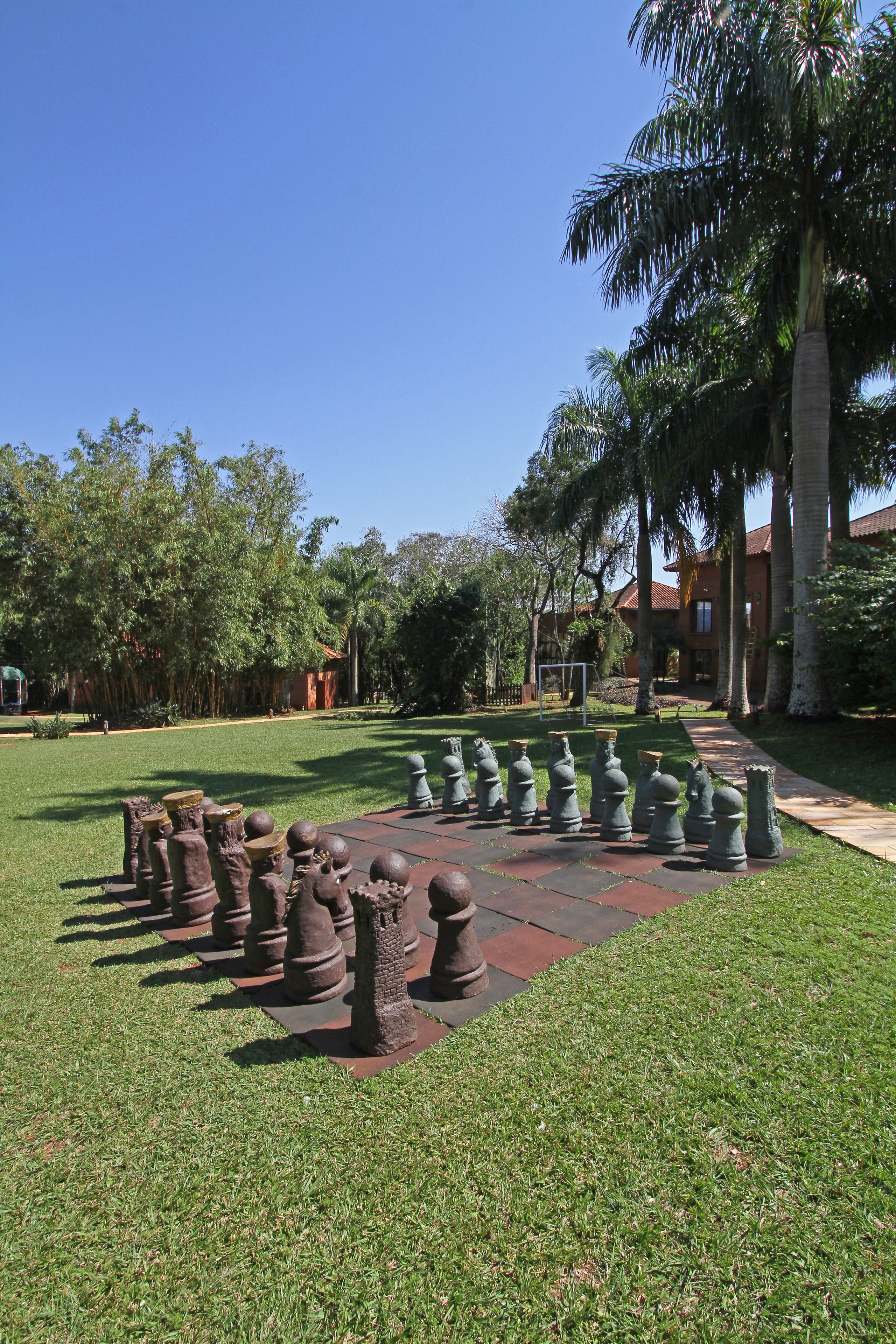 A courtyard with a chessboard arrangement of sculptures, surrounded by palm trees and a building with a red roof.