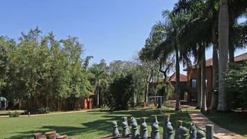 A courtyard with a chessboard arrangement of sculptures, surrounded by palm trees and a building with a red roof.
