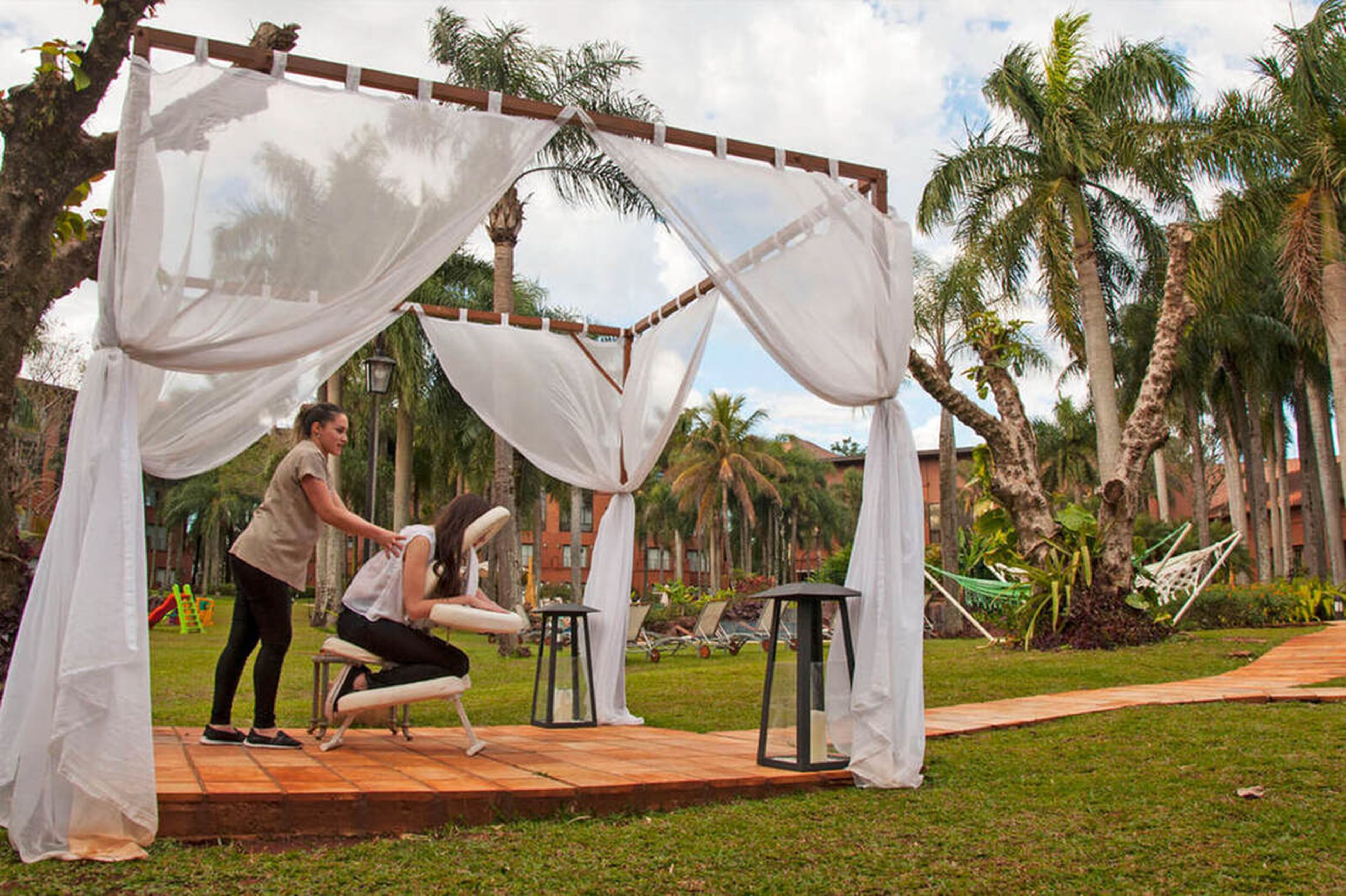A gazebo with white drapes in a tropical setting with palm trees and a hammock.