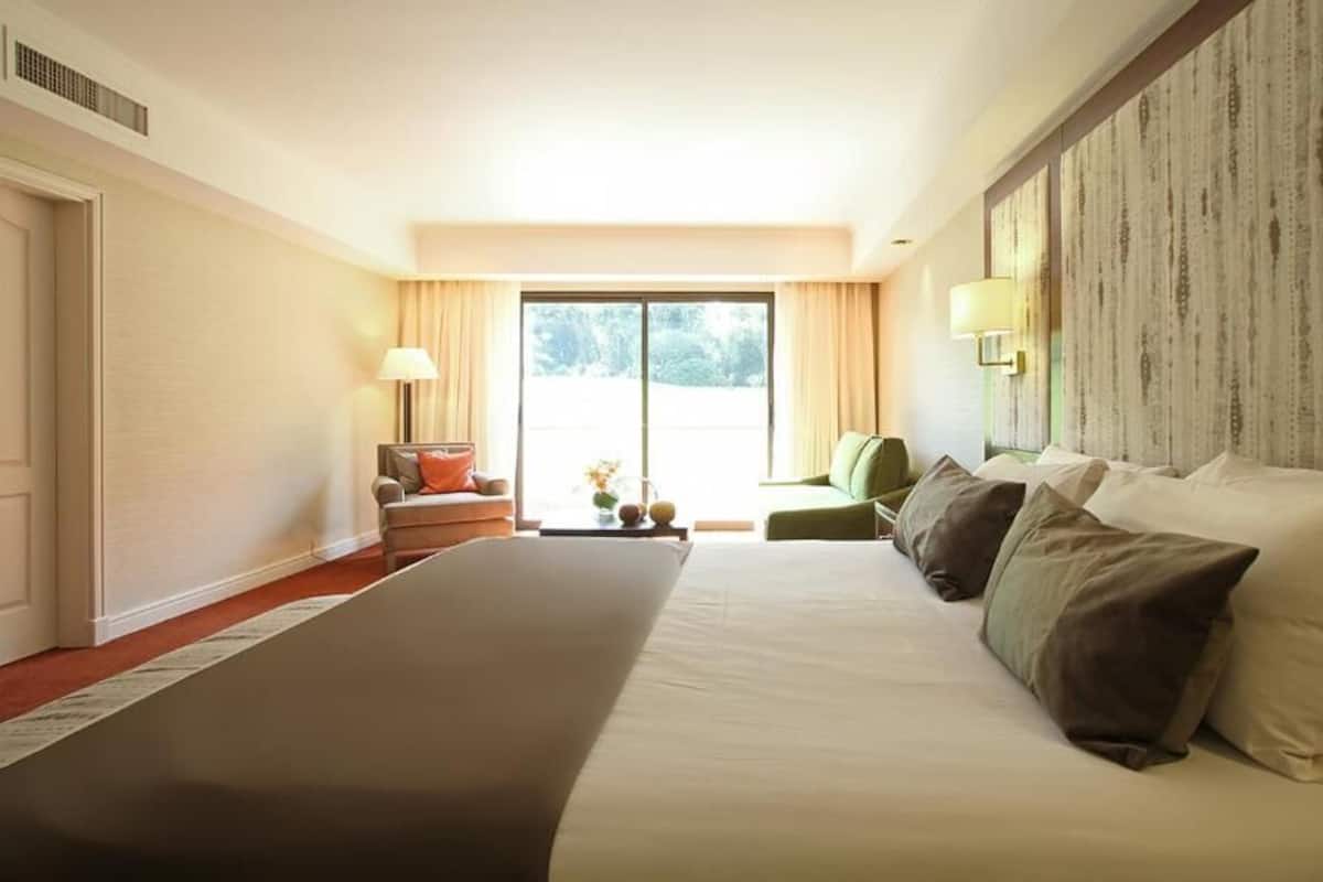 Une chambre d’hôtel dotée d’un grand lit, d’un coin salon avec un fauteuil et une table, d’une grande fenêtre et d’un mur au motif texturé.
