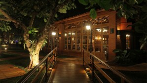 A wooden bridge leading to a building with large windows and a brick facade at night. - Iguazu Grand Resort Spa & Casino (Puerto Iguazú)