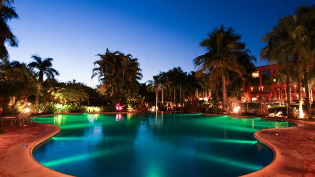 A nighttime view of a swimming pool surrounded by palm trees and a building with illuminated windows. - Iguazu Grand Resort Spa & Casino (Puerto Iguazú)