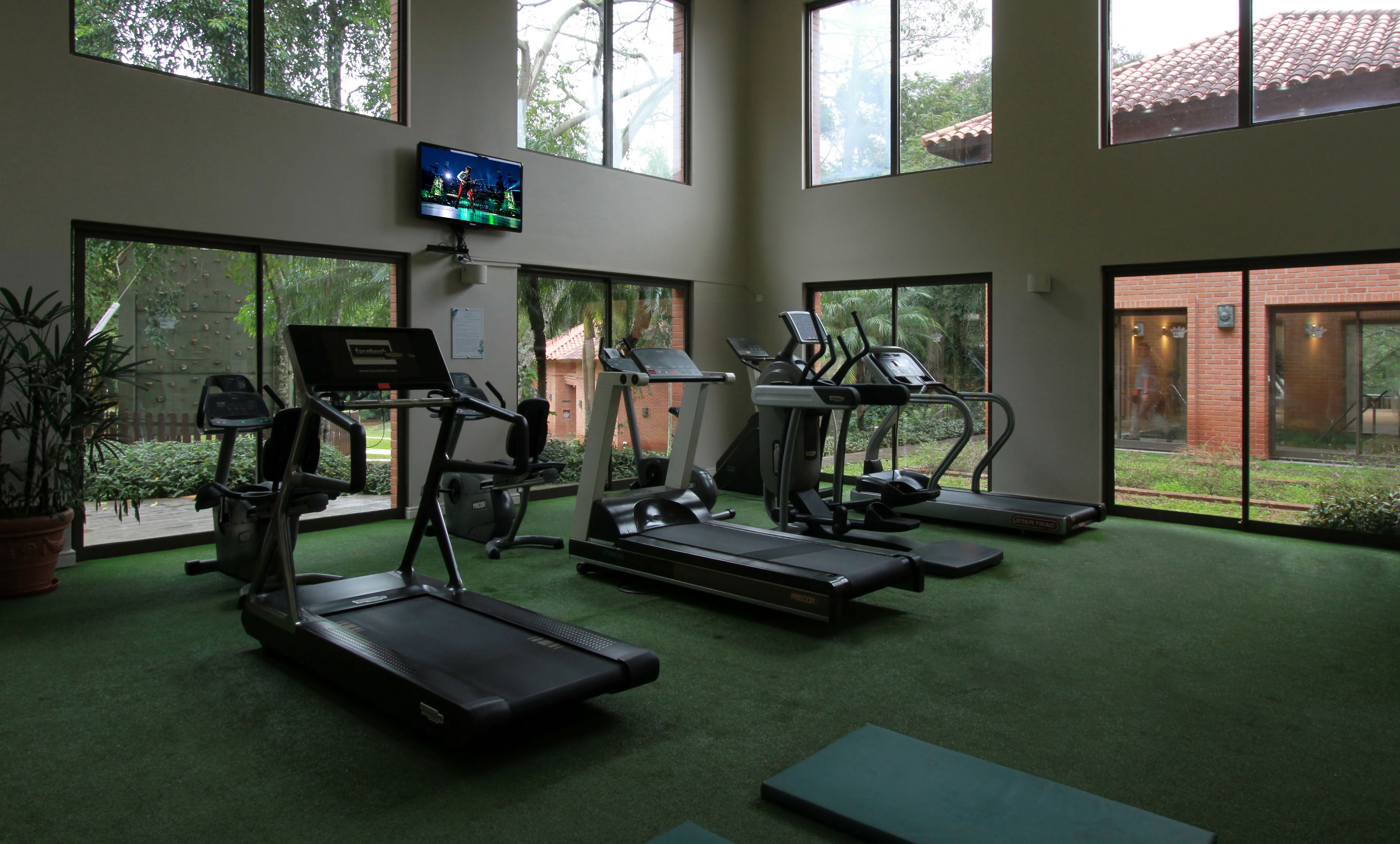 Une salle de sport équipée de tapis de course, de vélos elliptiques et d’un écran de télévision.