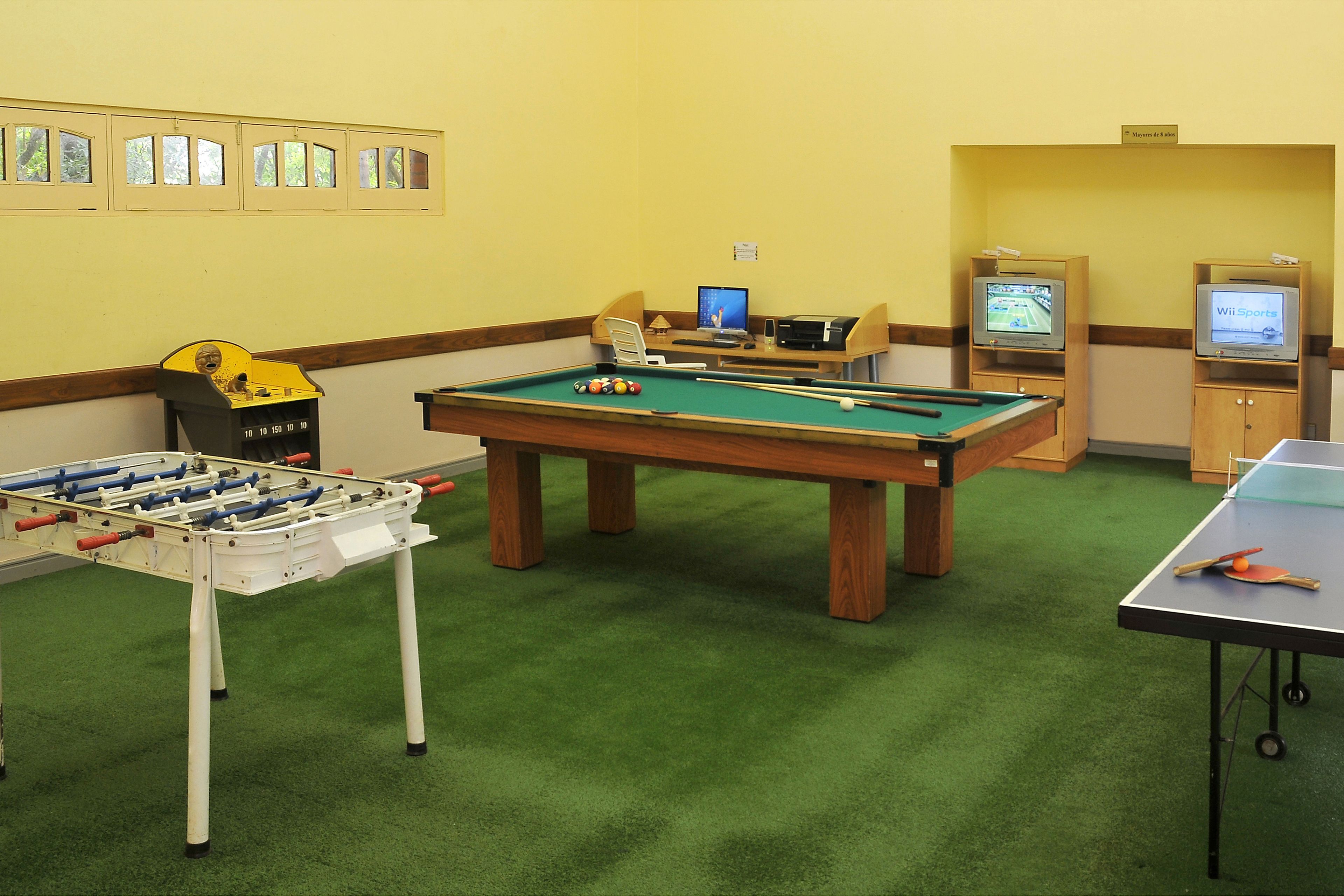Une pièce équipée d’une table de billard, d’un baby-foot et de deux téléviseurs diffusant des programmes sportifs.
