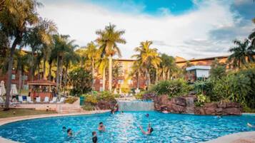 Relax by the pool surrounded by lush greenery and tropical plants, with lounge chairs and umbrellas nearby.