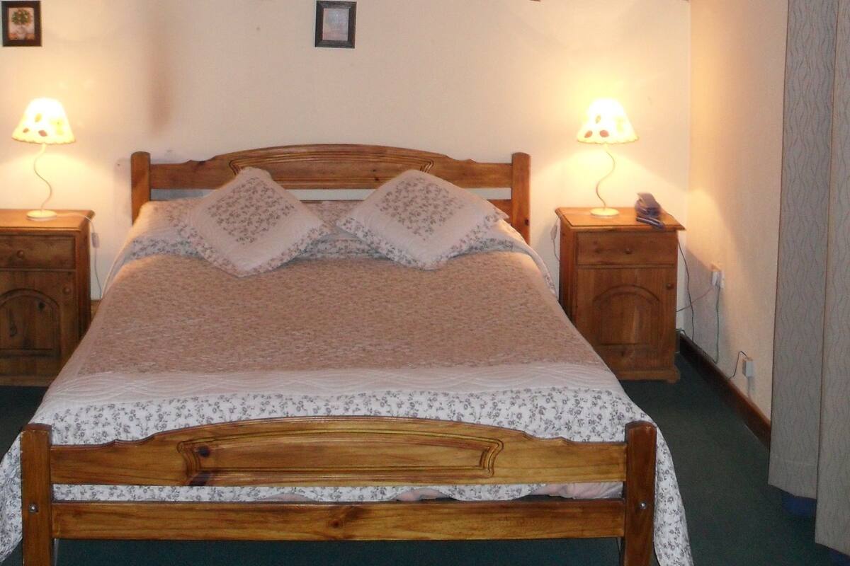 Een kamer met houten frame, een bed, twee bedlampen en een plafondlamp.