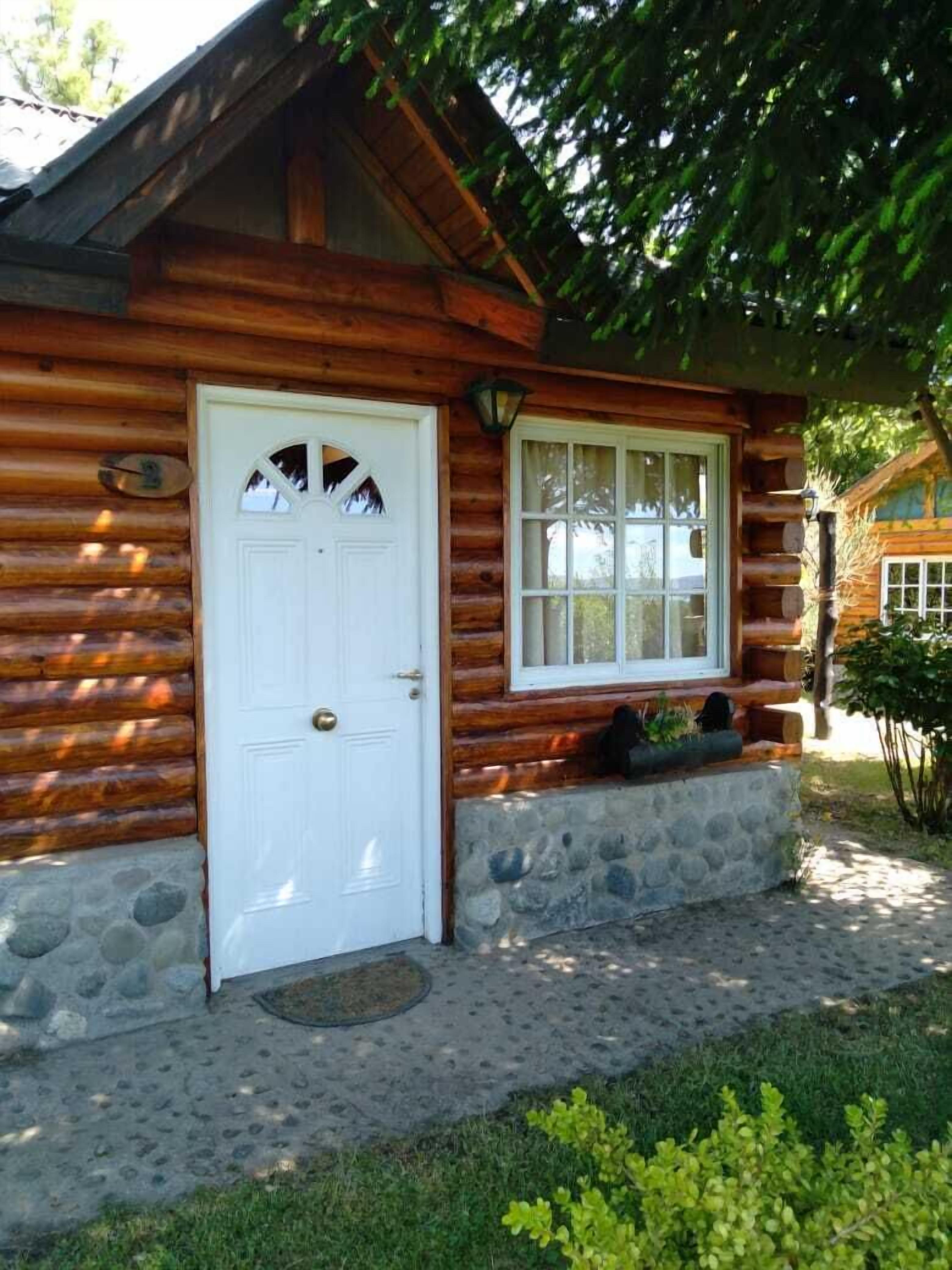 A log cabin with a white door and window, stone foundation, and a small porch area.
