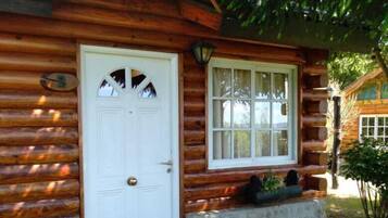 A log cabin with a white door and window, stone foundation, and a small porch area.