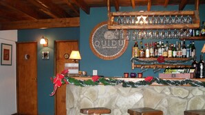 Un espace bar avec un comptoir en pierre, des tabourets en bois, une guirlande de Noël et un mur orné d’une enseigne « QUIDU ».