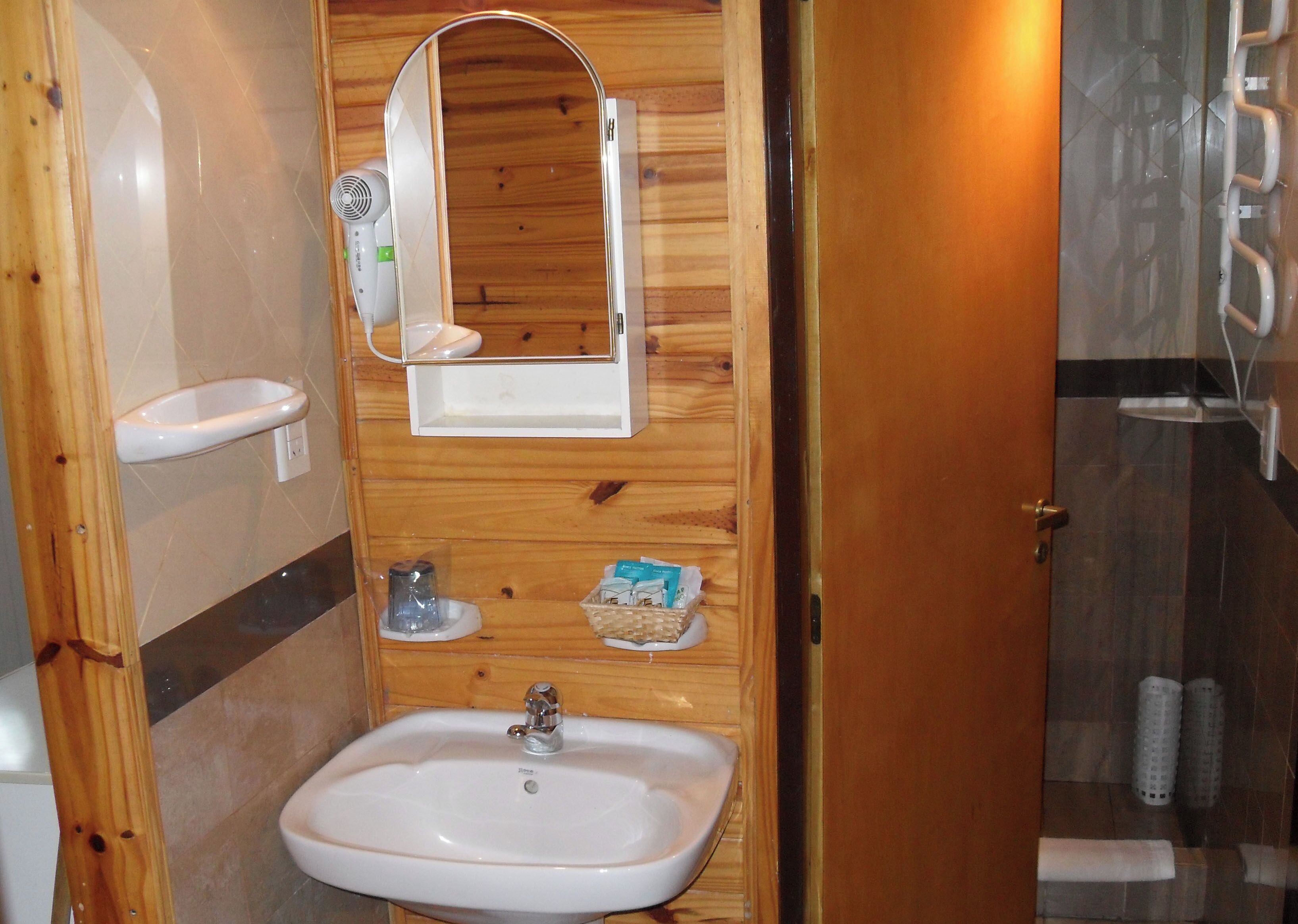 A compact bathroom with a wooden vanity, a sink, a mirror, and a shower area.