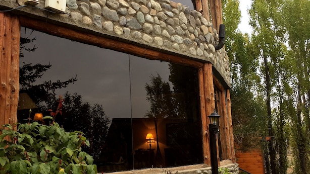 Un chalet rustique avec une façade en pierre, de grandes fenêtres et un revêtement extérieur en bois.