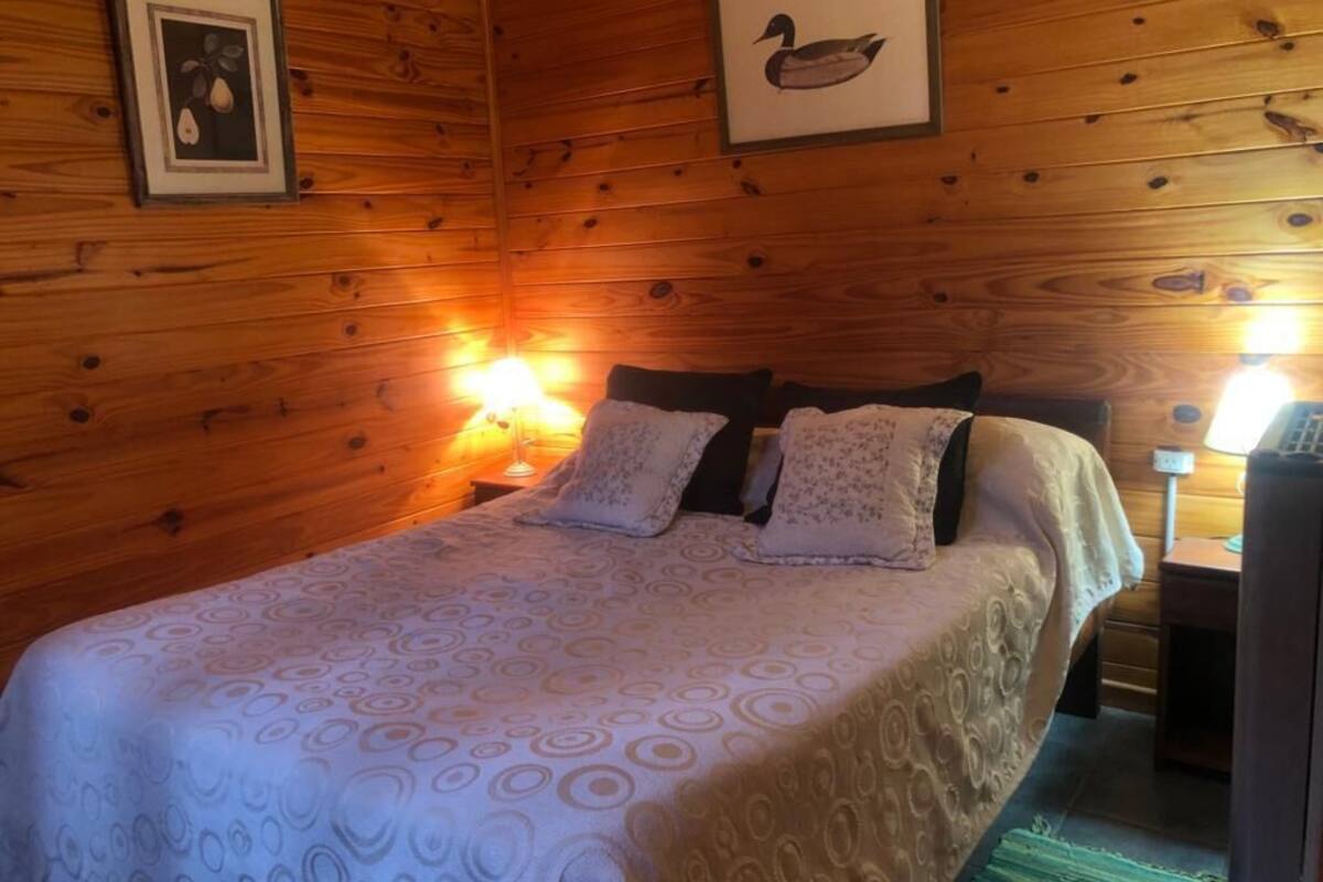 Een houten kamer met een bed, twee wandlampen en ingelijste foto's.