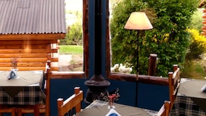 Une cabane en bois avec un coin repas comprenant une table dressée pour deux personnes, une lampe et une vue sur la verdure environnante.