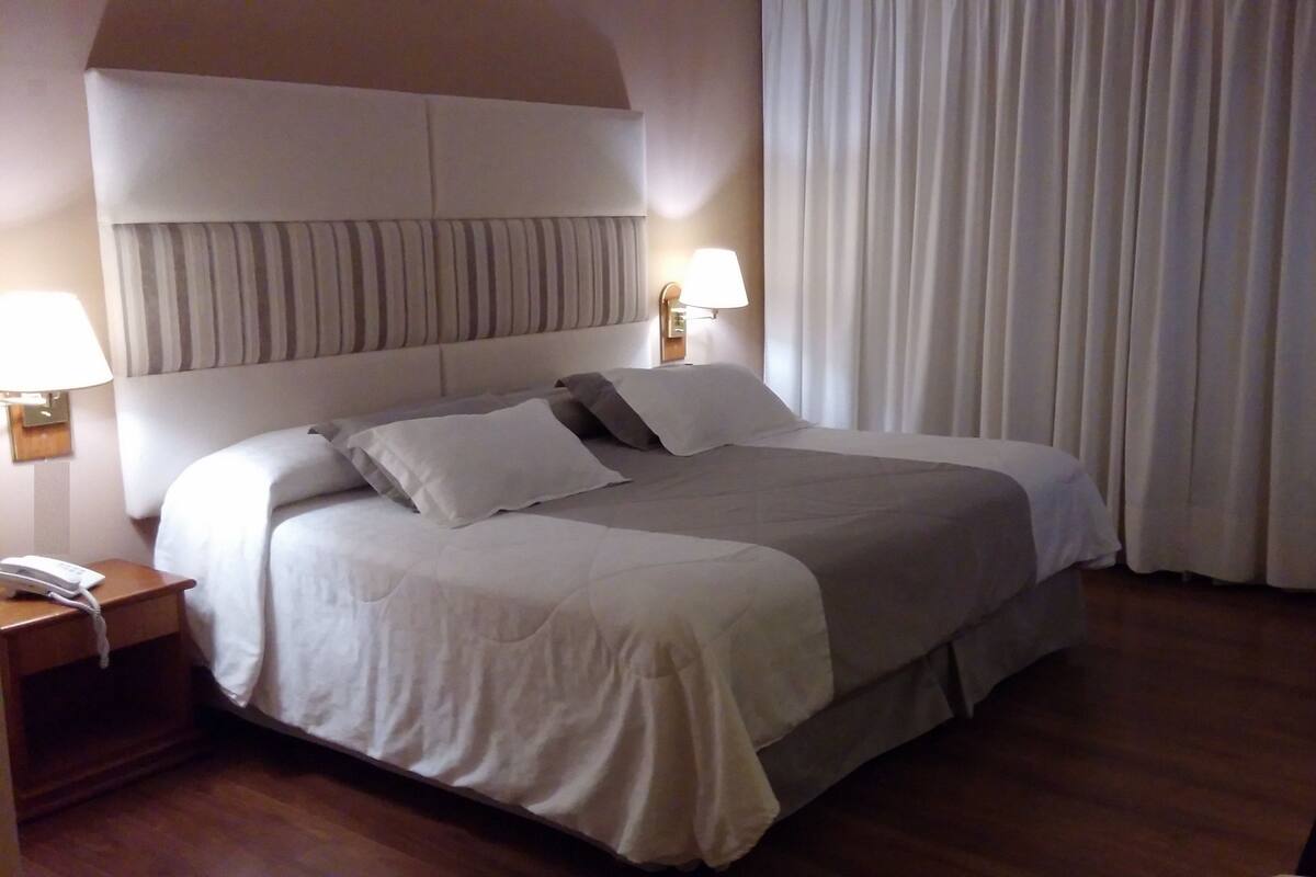 Quarto de hotel com uma cama grande, abajur, telefone e cortina.
