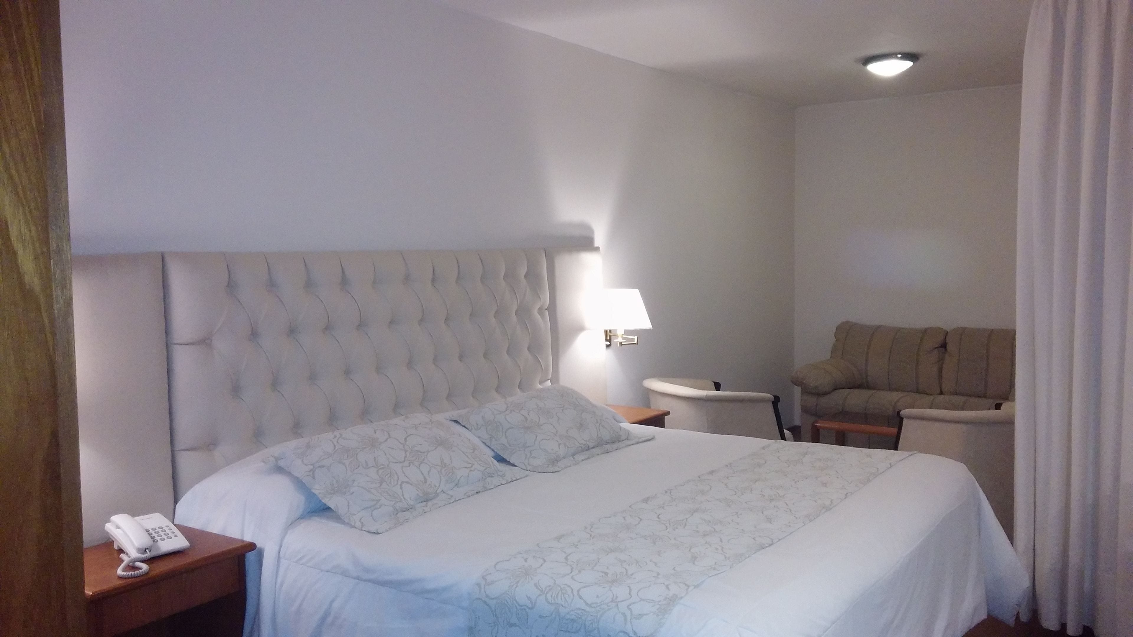 A hotel room with a large bed, a bedside telephone, a lamp, and a sofa.