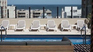 A poolside area with lounge chairs and a view of the ocean and buildings. - Hotel Remanso (Punta del Este)