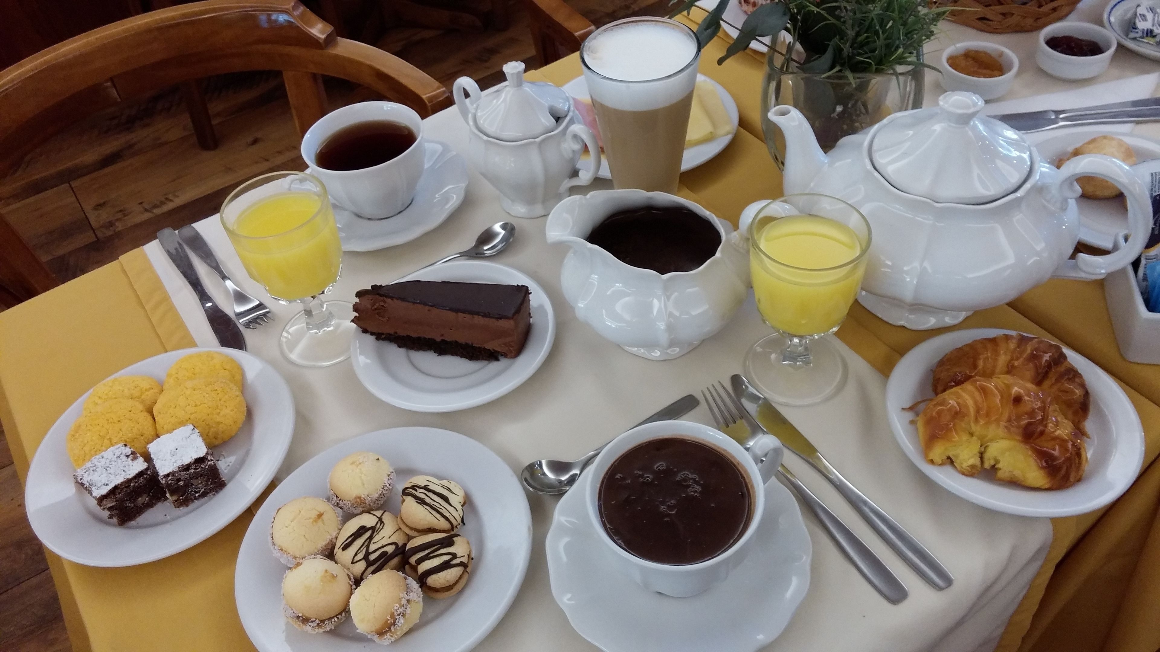 Taula de petit esmorzar amb diversos aliments, com ara pastissos, una porció de pastís de xocolata i tasses de cafè i suc.