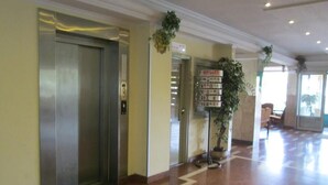 A hotel lobby with a marble floor, an elevator, a reception desk, and a plant. - Nap Hotel (Budapest)