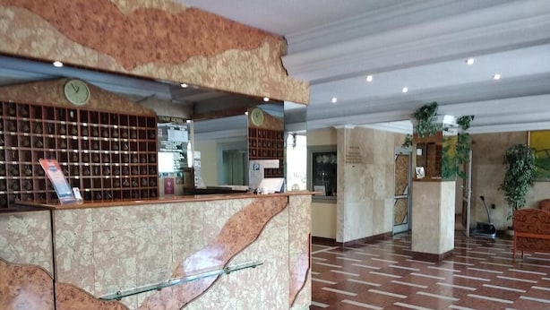 A hotel reception area with a marble counter, a clock, and a patterned floor. - Nap Hotel (Budapest)
