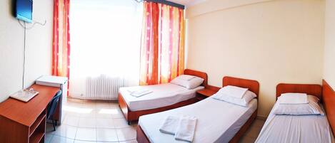 A hotel room with two single beds, a desk with a chair, and a window with curtains.