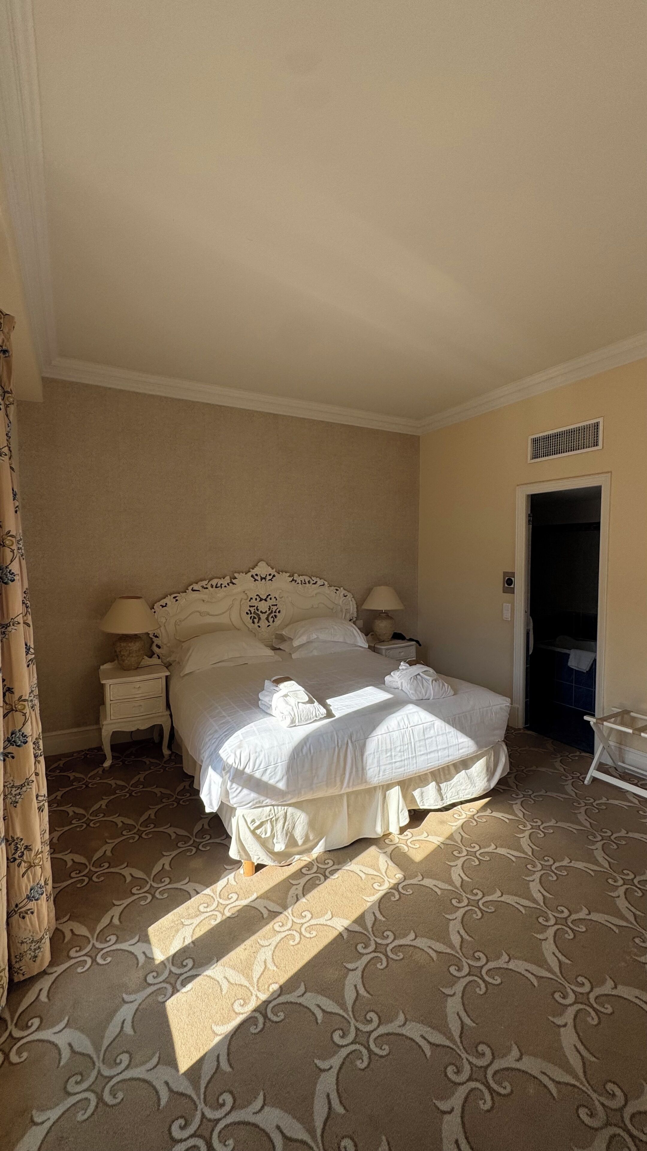 Una habitación de hotel con una cama grande, dos mesitas de noche con lámparas, una alfombra estampada y una puerta que da al baño.