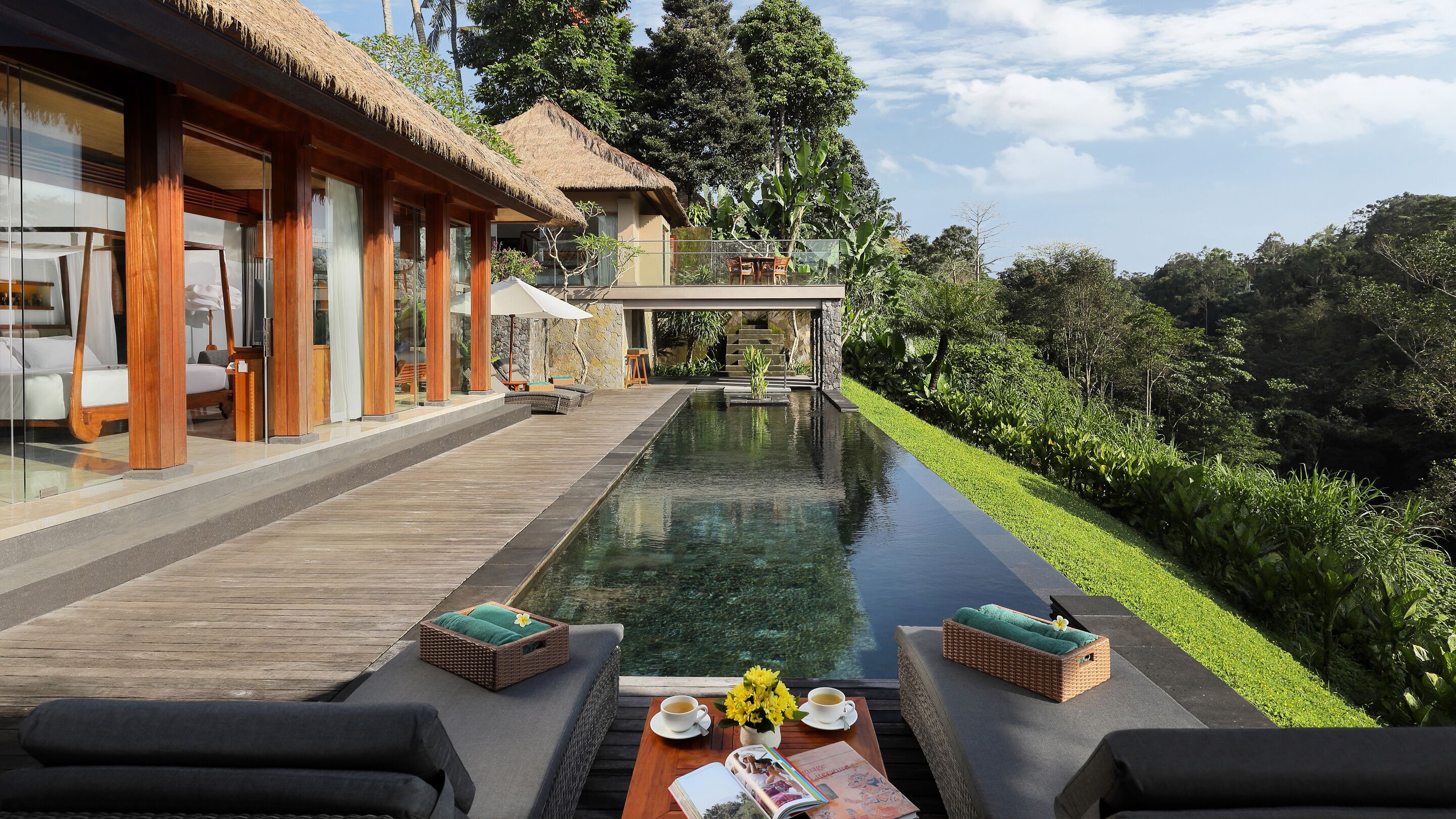 A modern resort with a swimming pool, wooden deck, and lush greenery.