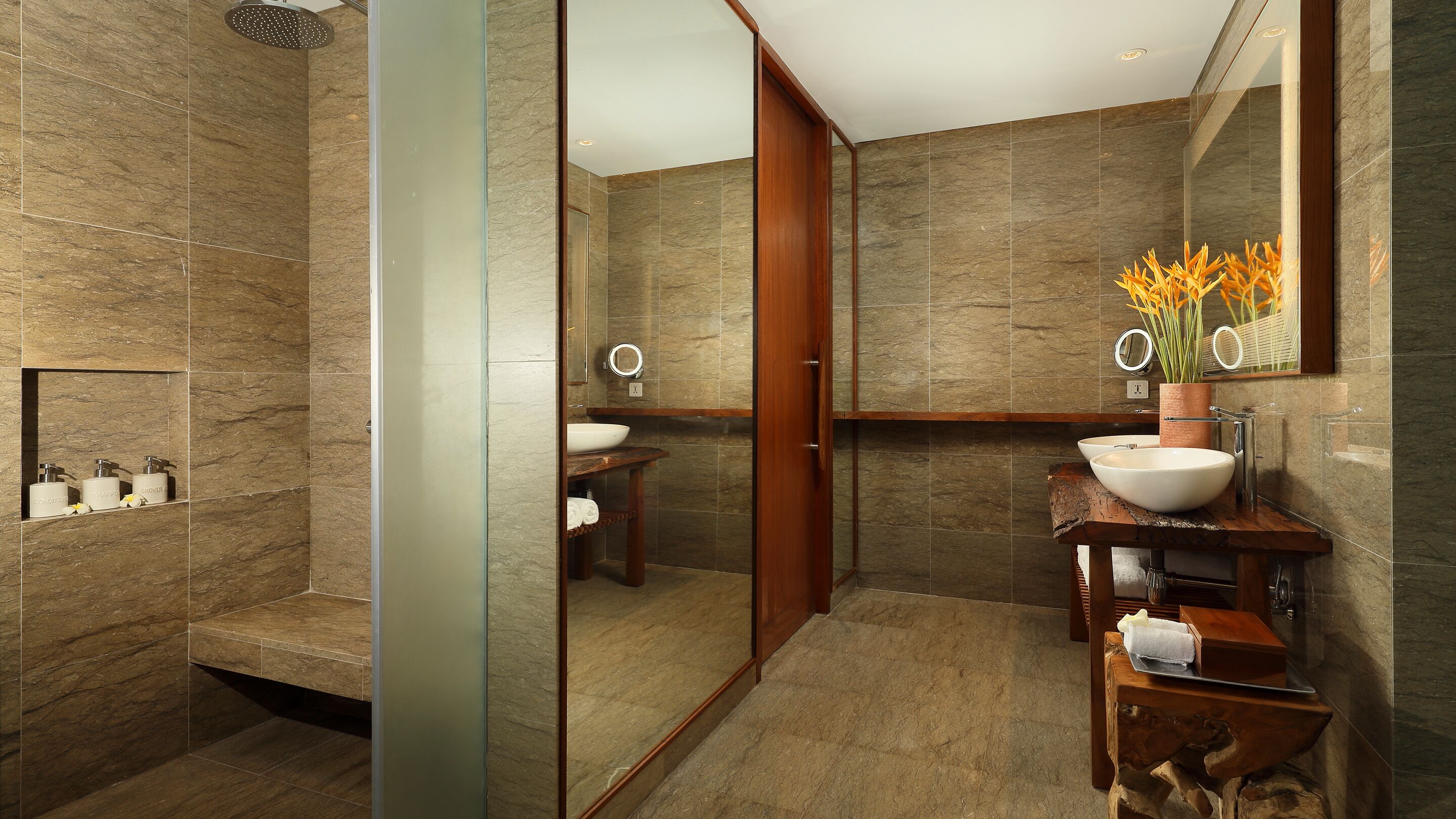 Un baño moderno con cabina de ducha de vidrio, tocador de madera con un lavabo grande y espejo sobre el tocador.