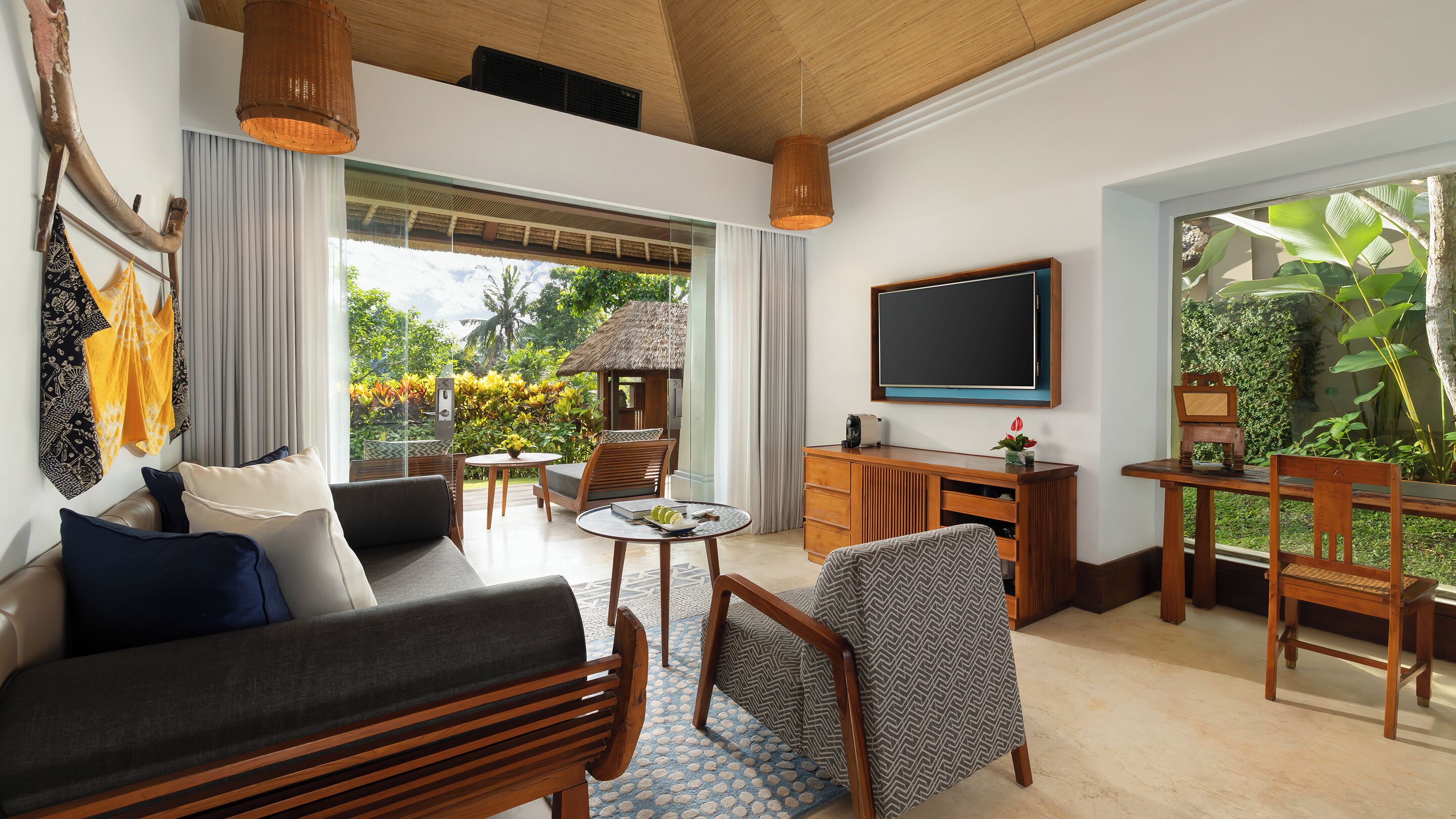 A modern living room with a sofa, chairs, a coffee table, a TV, and a view of a lush garden.