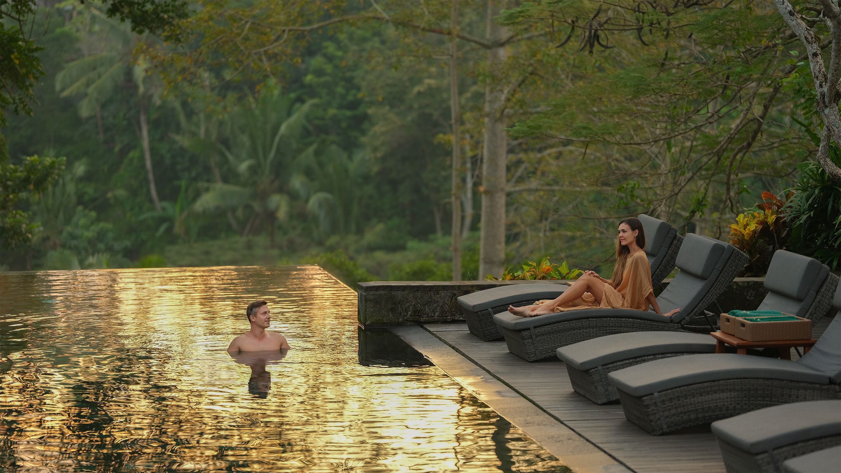 A poolside area with lounge chairs and a person in the water.