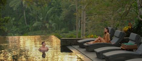 Zona de piscina con sillones reclinables y una persona en el agua.