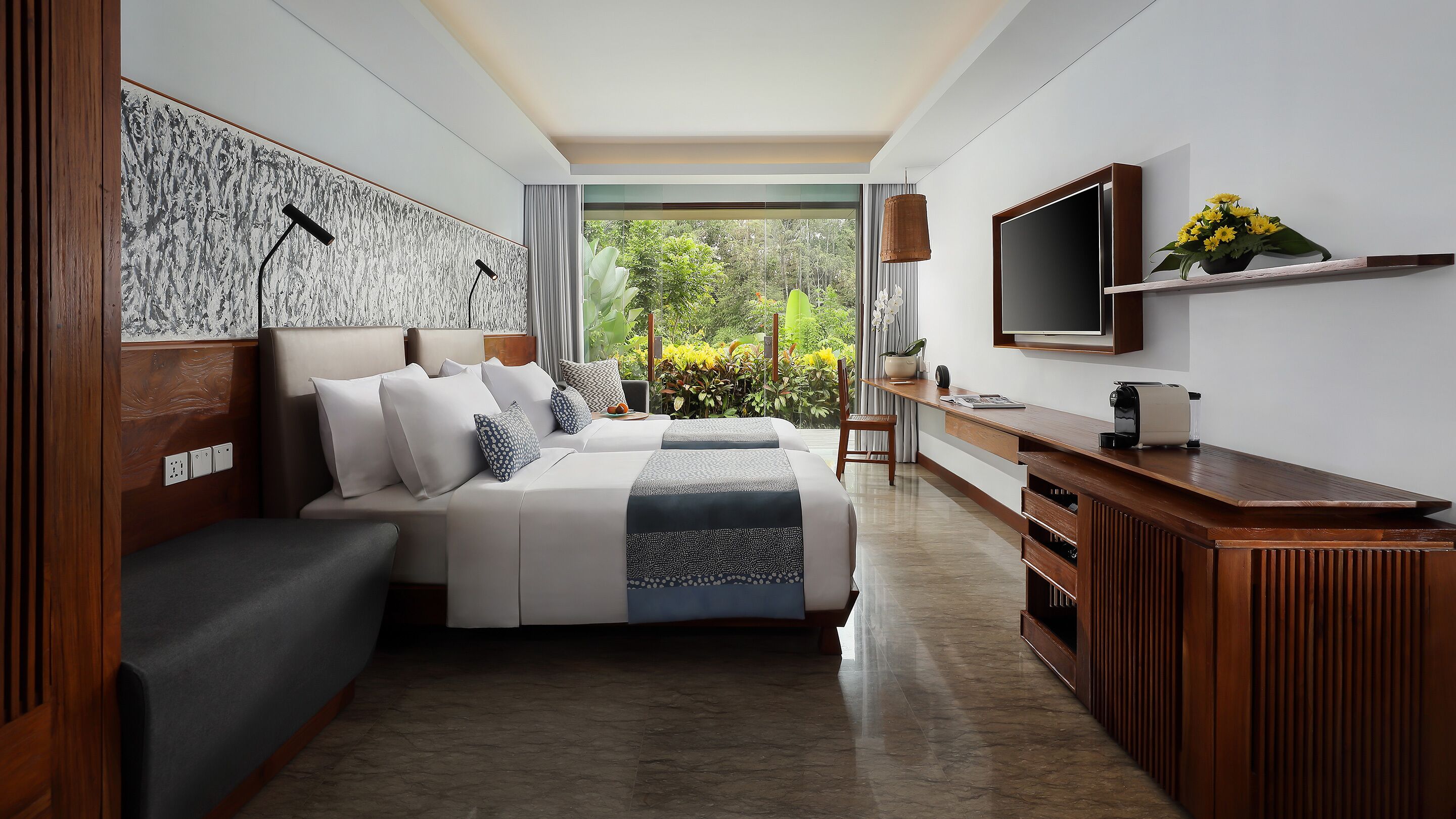 Quarto de hotel moderno com uma cama grande, televisão, escrivaninha de madeira e vista para o verde.