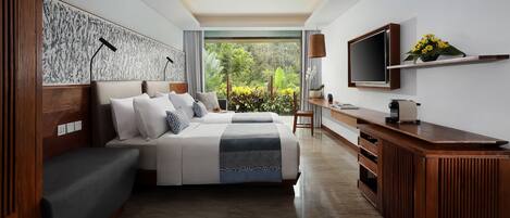 A modern hotel room with a large bed, a TV, a wooden desk, and a view of greenery.
