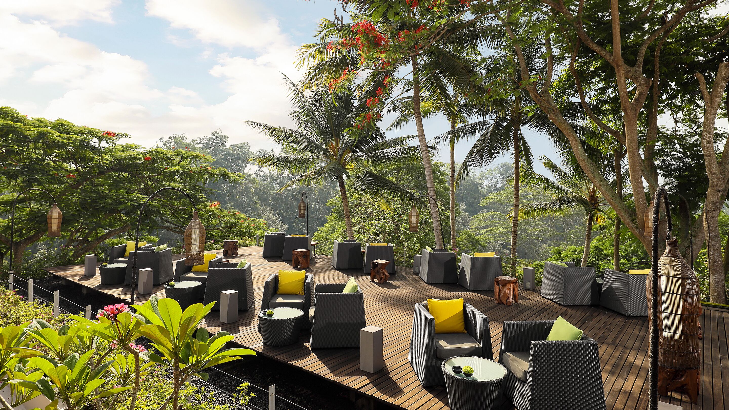 An outdoor deck with wicker furniture and a wooden floor, surrounded by lush greenery and trees.