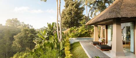 A modern villa with a thatched roof, a pool, and lush greenery surrounding it.