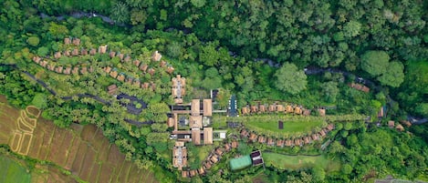 An aerial view of a resort with a central building surrounded by guest villas, a golf course, and agricultural fields.