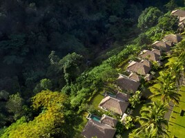 An aerial view of a resort with thatched-roof cottages, lush greenery, and a swimming pool.