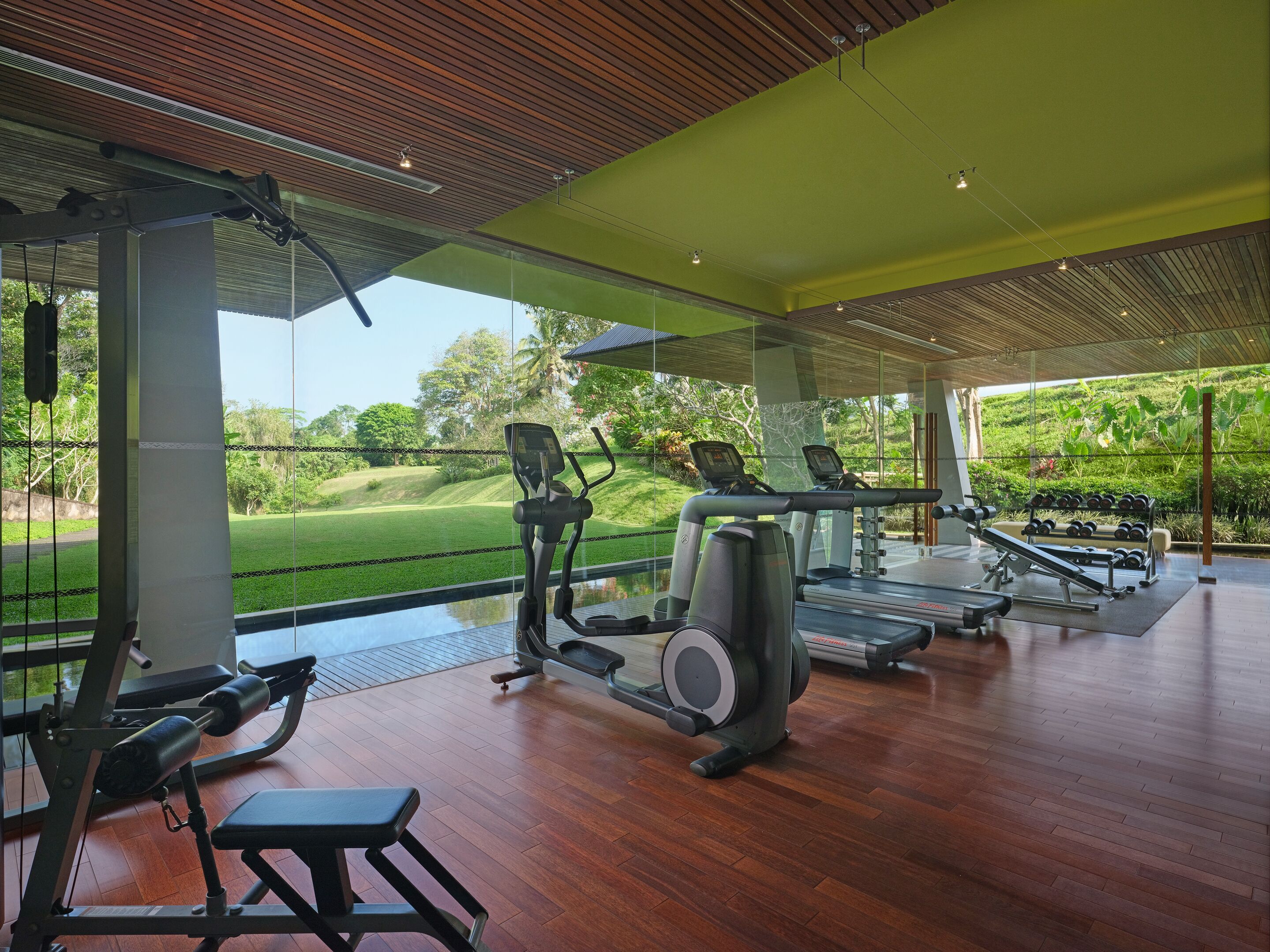 A modern gym with exercise equipment, large windows, and a view of a green landscape.