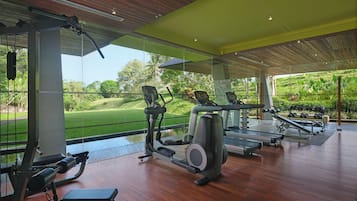 A modern gym with exercise equipment, large windows, and a view of a green landscape.